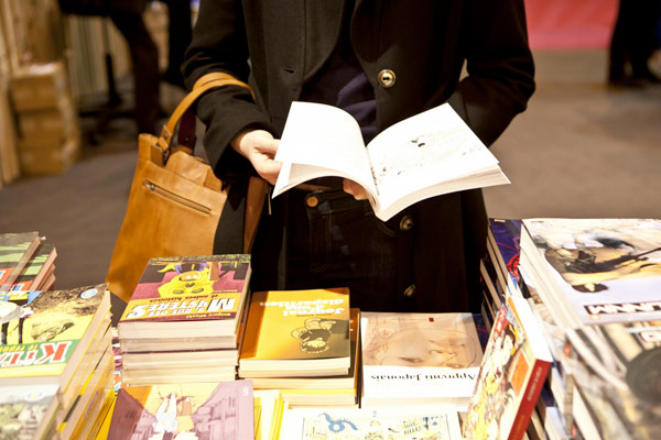 Le salon du livre : l’occasion de (re)découvrir le Petit Prince de Saint-Exupéry Femme feuilletant un livre présenté parmi d'autres