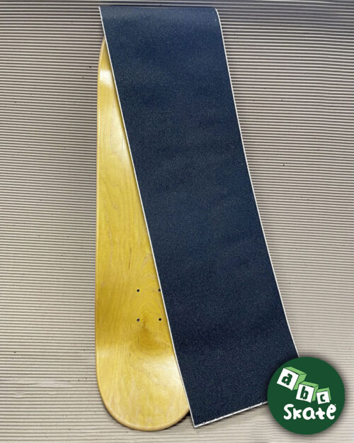 Grip noir de la marque Jessup à côté d'une planche de skate "vierge"
